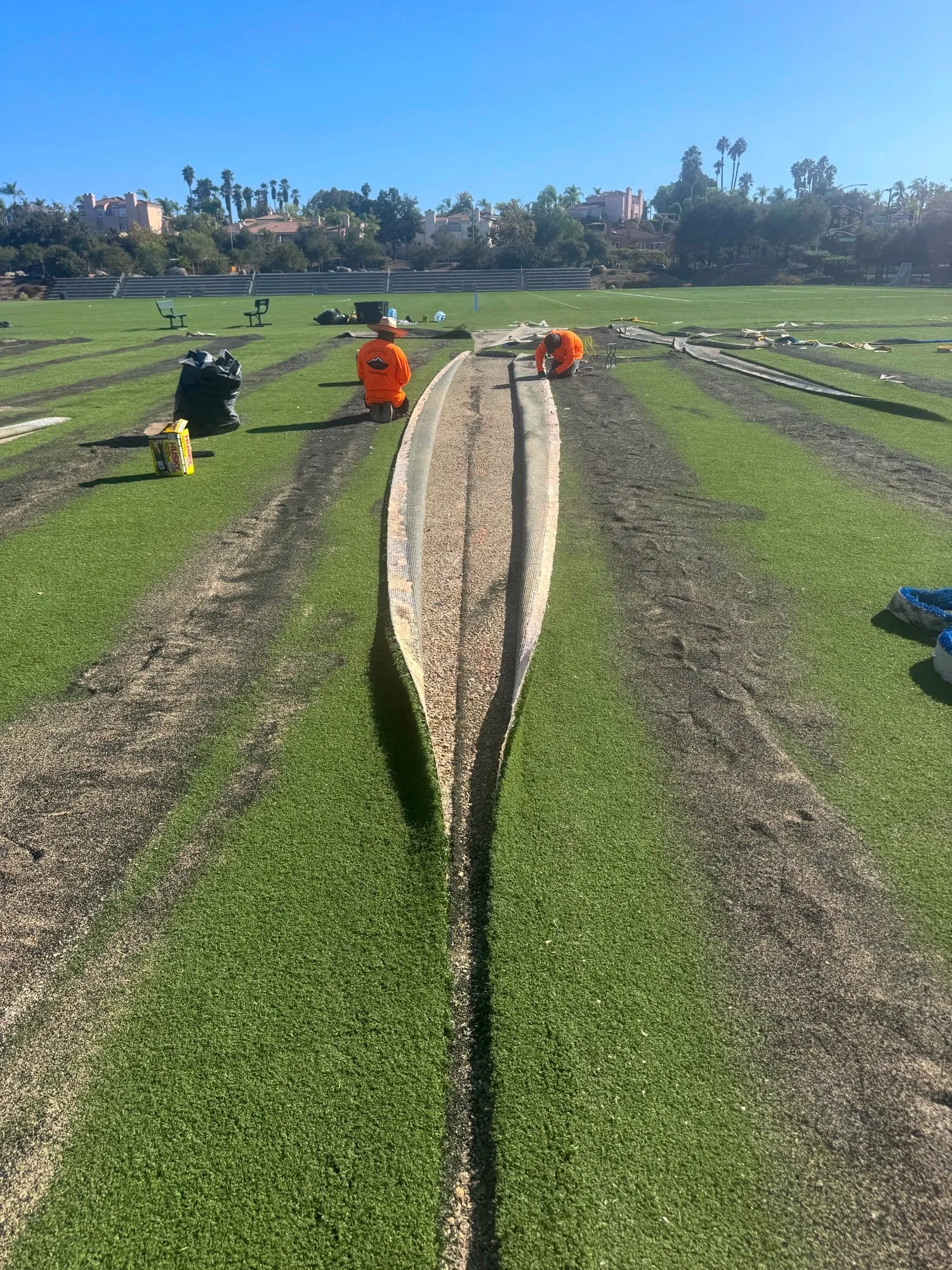 Two crew members kneeling at an open seam with both turf edges folded back